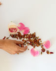 Hand interacting with pink rose petals and dried flowers on a white surface