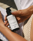 A person holding a black pump bottle of Ives & Bees Plant-Based Body Lotion. The bottle has a white label with black text.