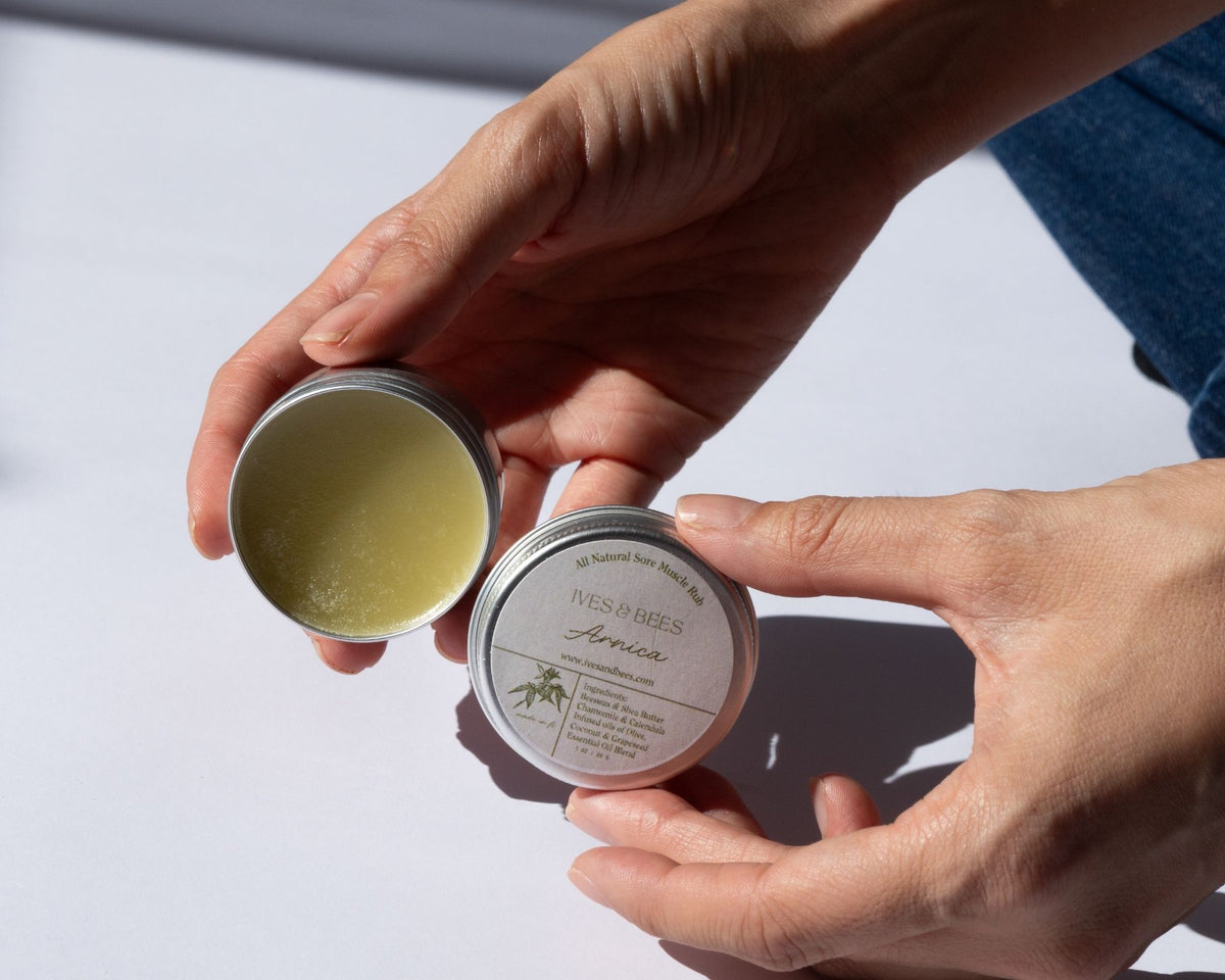 Two hands holding Arnica Salve  against a light background.