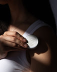 Person holding Arnica Salve with a label, wearing a white tank top.