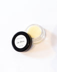 A small open jar of lip balm with pale yellow balm visible inside, next to its black lid which has a white label reading 'Ives & Bees Lip Balm'.
