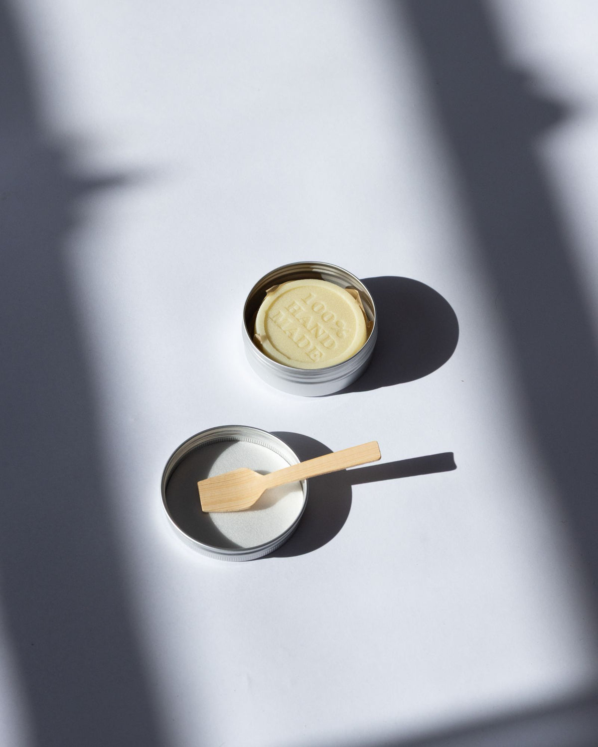 Chamomile and Calendula Lotion Bar with a wooden spatula on a light surface, casting shadows.
