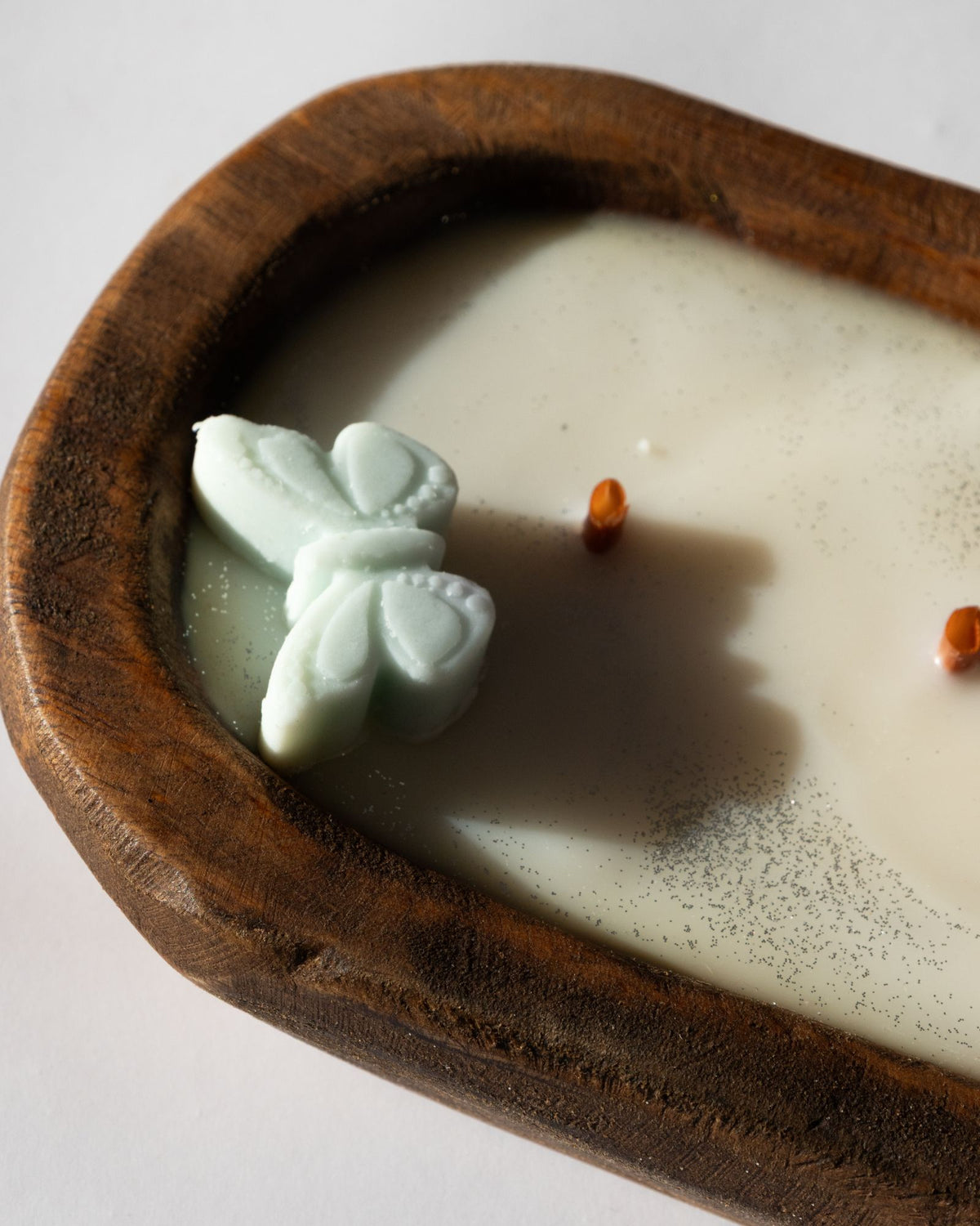 Butterfly-shaped soap in a wooden bowl with a candle