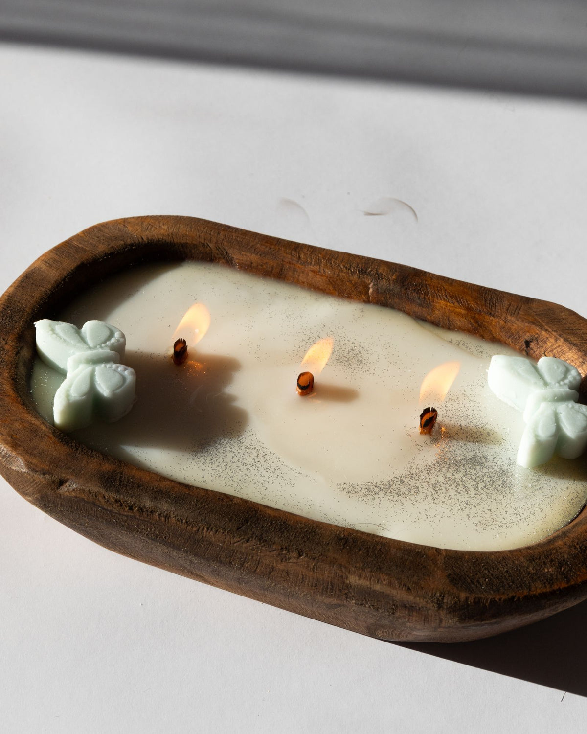 Diwata Wooden Bowl Candle with butterfly-shaped wicks in a wooden holder on a white surface