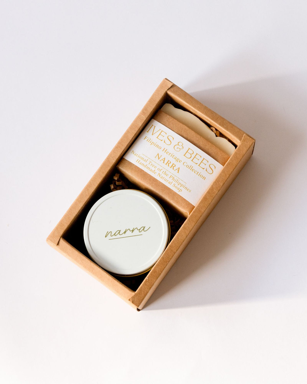 A gift set from Narra & Bee's 'Original Heritage Collection' in a brown kraft paper box, featuring a round white tin with a gold 'narra' logo and a wrapped bar of honey with a cream label.