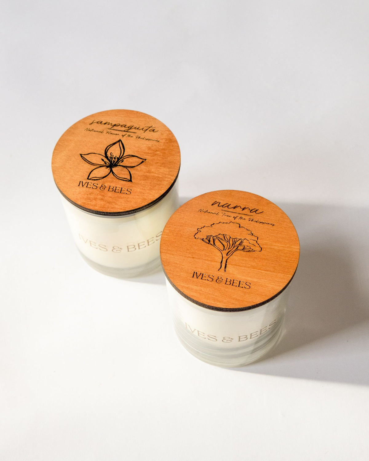 Sampaguita Candle & Narra Candle Duo with round engraved wooden lids, photographed on a clean white background. 
