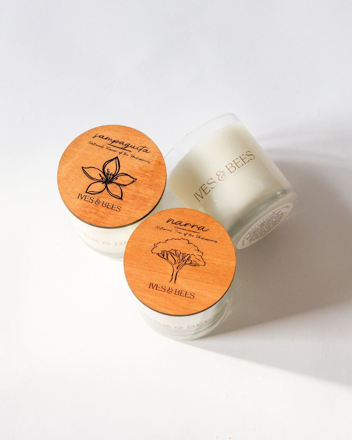 Sampaguita Candle & Narra Candle Duo with round engraved wooden lids, photographed on a clean white background. 